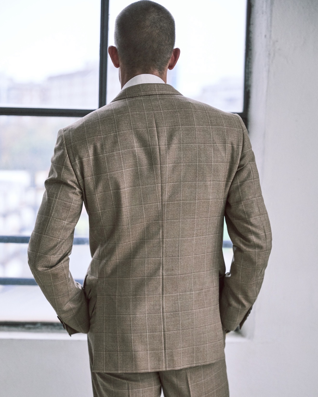 Man in a checked Pal Zileri suit viewed from behind, looking out a large window